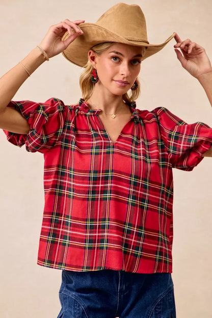 Red and green plaid holiday blouse with short ruffled sleeves, a soft flowy silhouette, and a narrow V-neck opening.